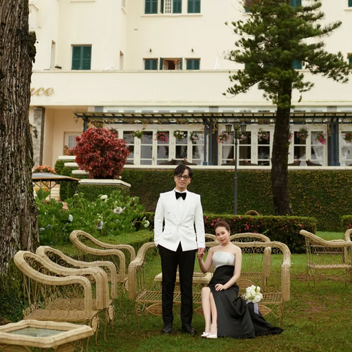 The bride sitting beside the groom in front of the hotel grounds.