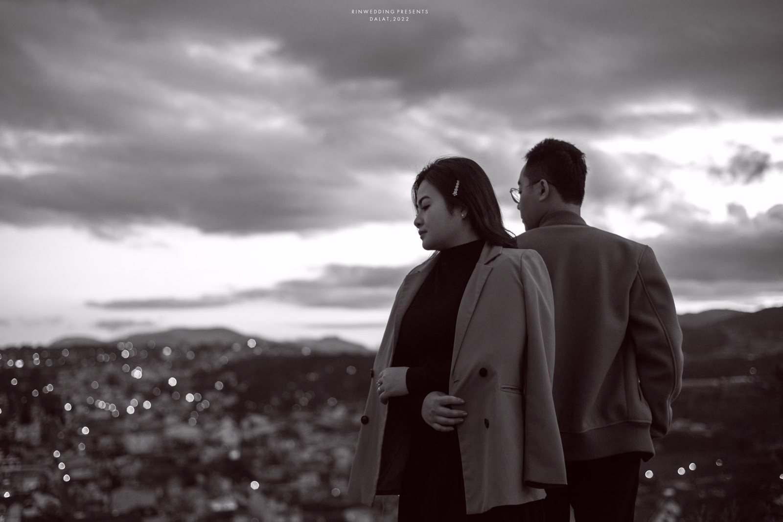 Black-and-white photograph of the couple with their backs to the camera, overlooking the city.