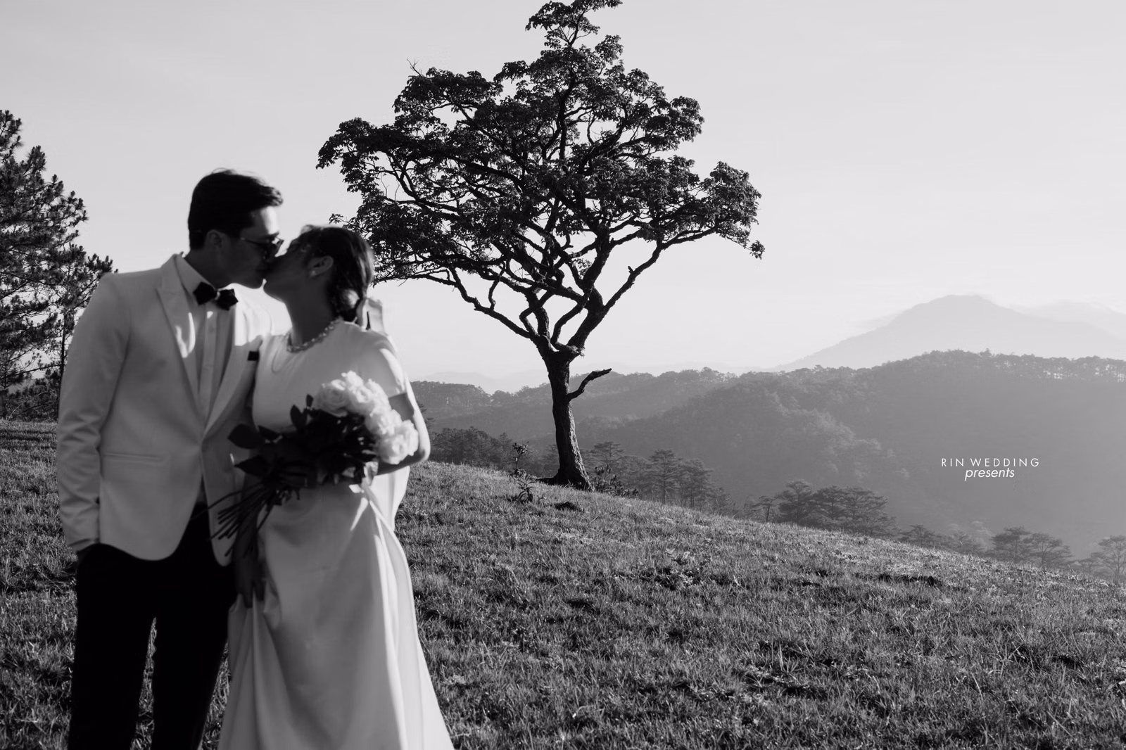 Black-and-white photograph of a couple beside a tree on a hill at Đồi Thông Đà Lạt