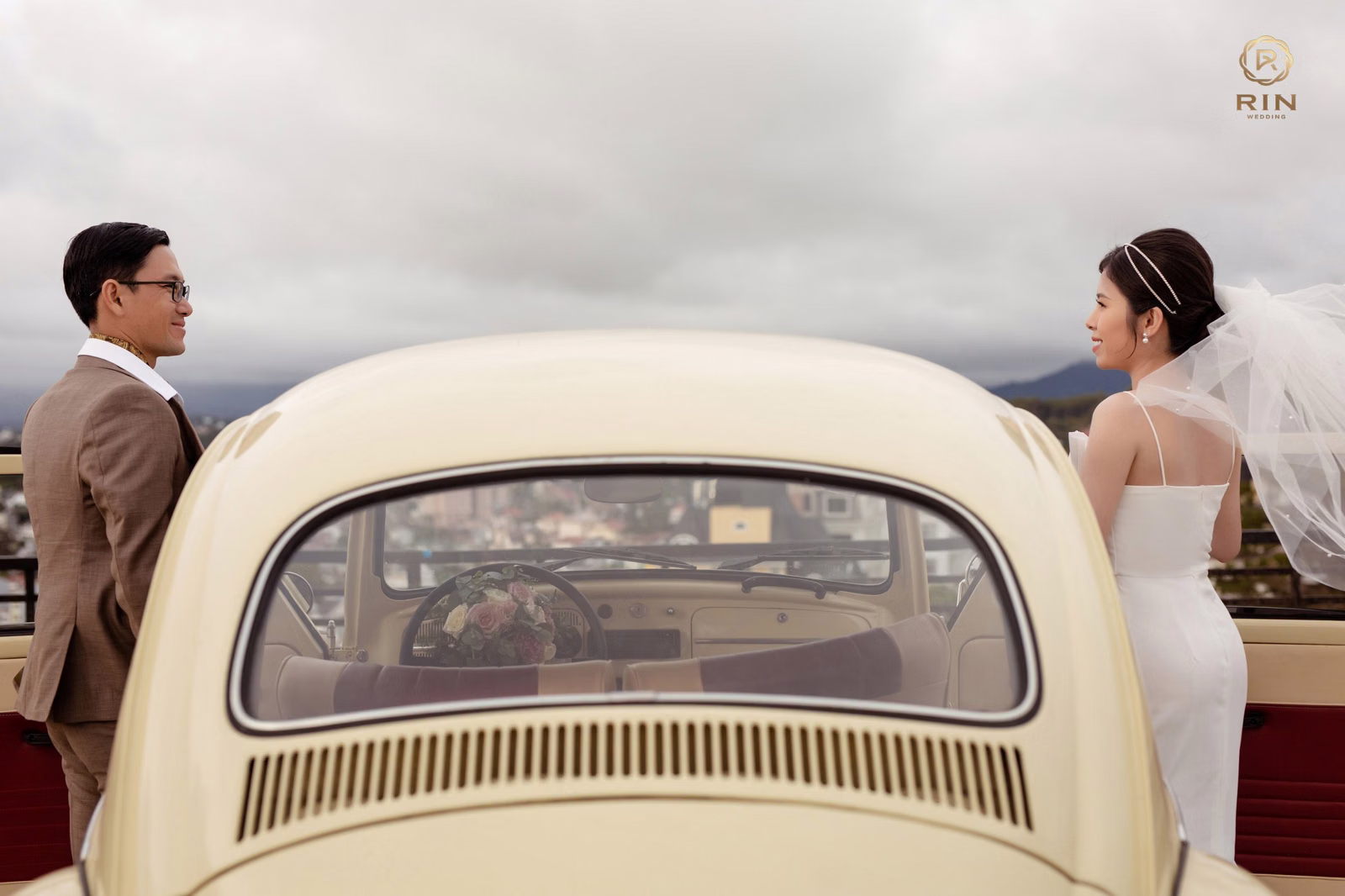 The couple on opposite sides of an ivory vintage car, looking at each other.