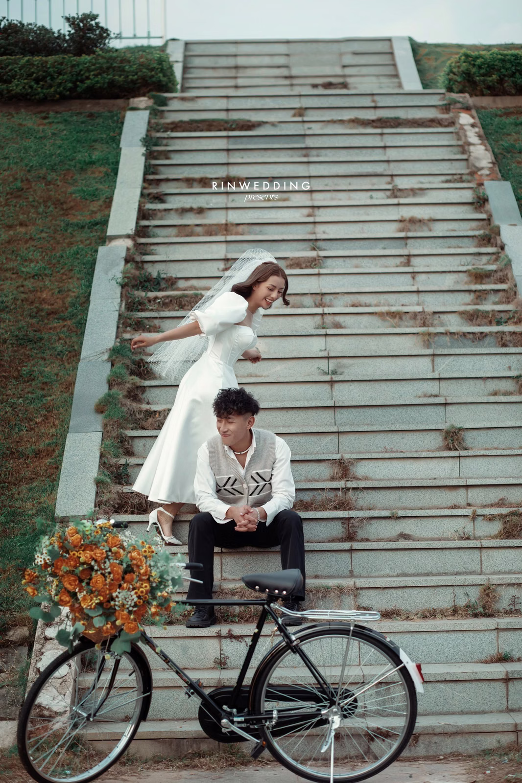 A couple with a flower-decorated bicycle on the steps at Công Viên Ánh Sáng.