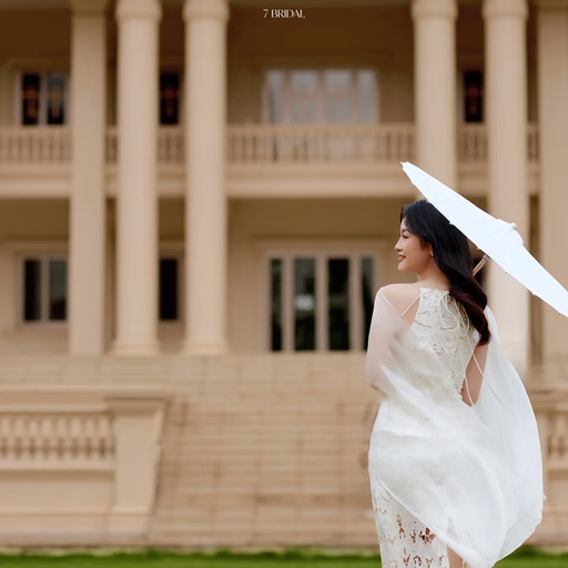 A bride holds a white parasol on the lawn at Nhà thờ Don Bosco