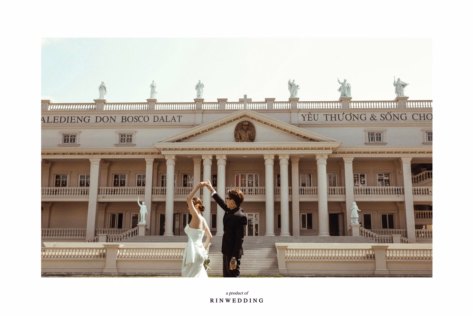 The groom raising the bride’s hand before the façade of Nhà thờ Don Bosco