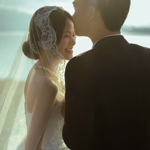 The groom kissing the veiled bride's forehead beside the lake at Cây Thông Cô Đơn, Đà Lạt