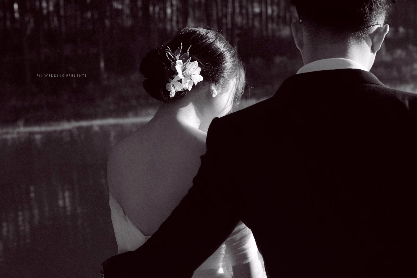 Black-and-white wedding photograph of the couple looking towards a lake.