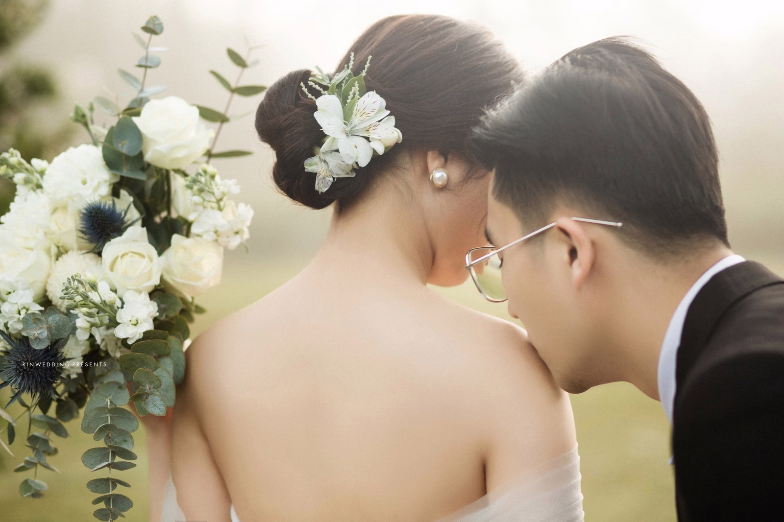Close-up of a groom kissing the shoulder of a bride with white flowers in her hair.