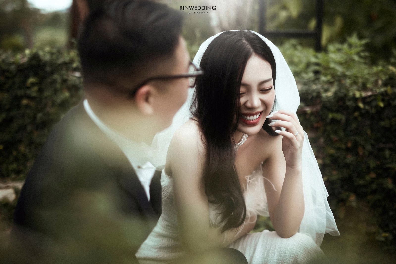 The bride smiling beside the groom in a resort garden.