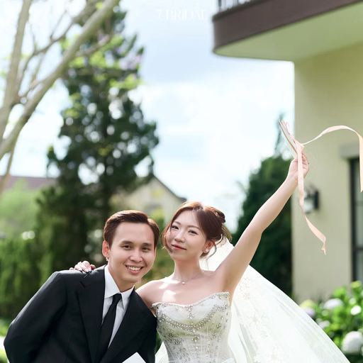 The bride raises her hand joyfully beside the groom holding a wedding invitation in the garden.