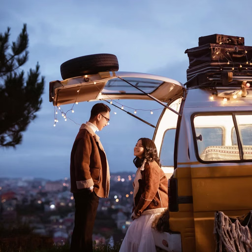 The couple stands beside the door of a camper van beneath the twilight sky.