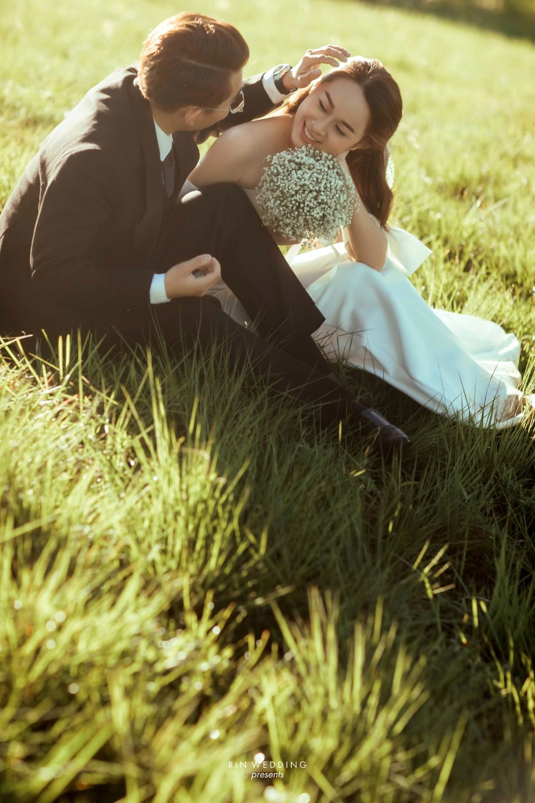 The couple sits leaning together on grass at Đồi Thông Đà Lạt