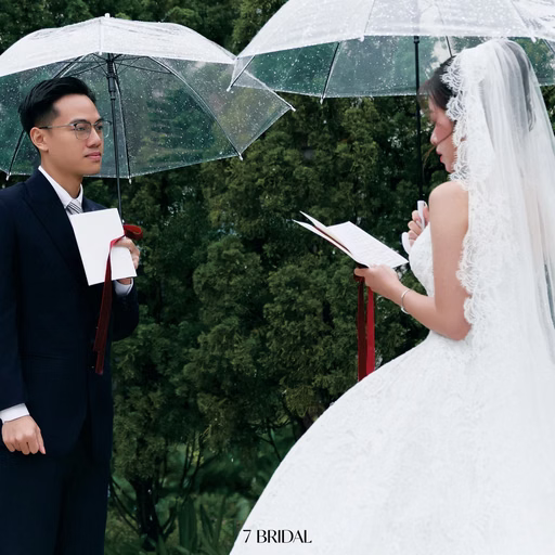 The bride reading a message to the groom beneath an umbrella in a garden.