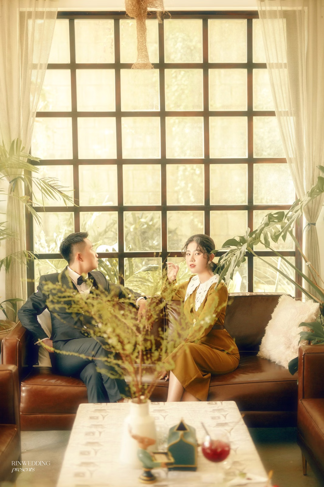 The couple chats on a sofa beside a large window in a Đà Lạt café.