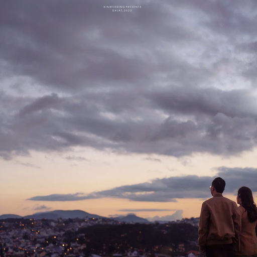 A couple looking out over Đà Lạt under a cloudy evening sky.