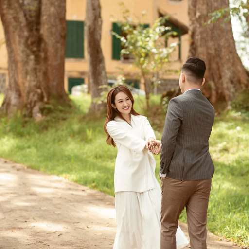 A couple holds hands on the path before the yellow mansion at Dinh Tỉnh Trưởng.