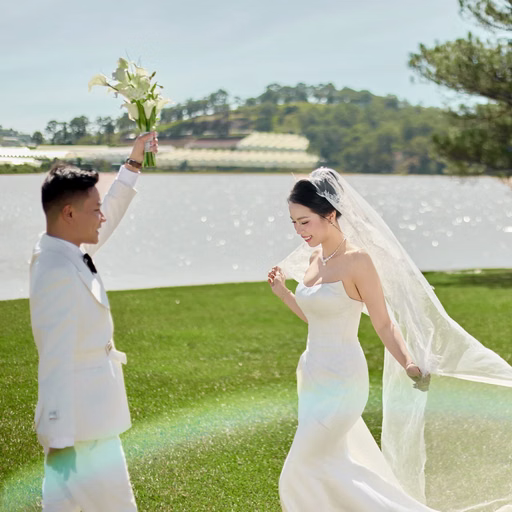 The groom raising a bouquet and holding the bride's hand beside the lake at Cây Thông Cô Đơn, Đà Lạt