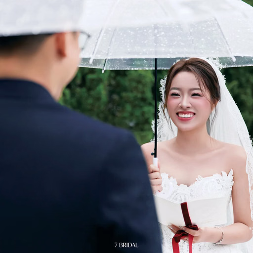 The bride smiles at the groom beneath a clear umbrella.