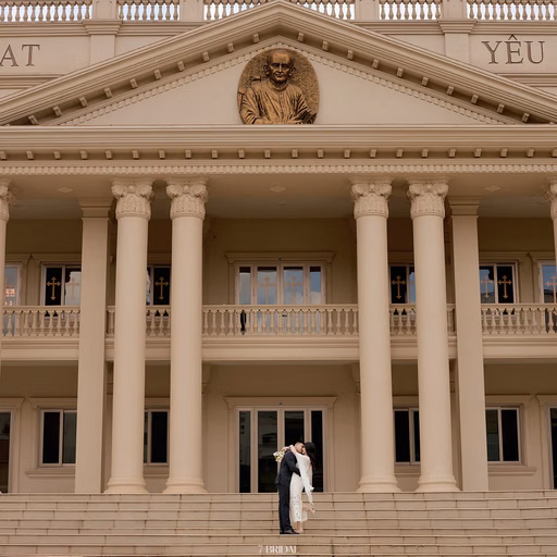 A bride and groom stand beneath the façade of Nhà thờ Don Bosco