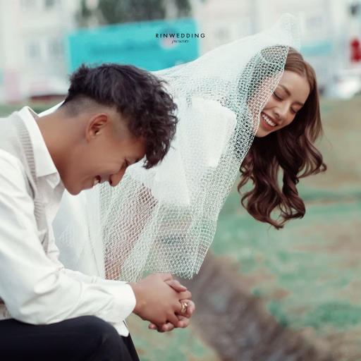 The groom bowing his head beside the bride beneath a white veil.