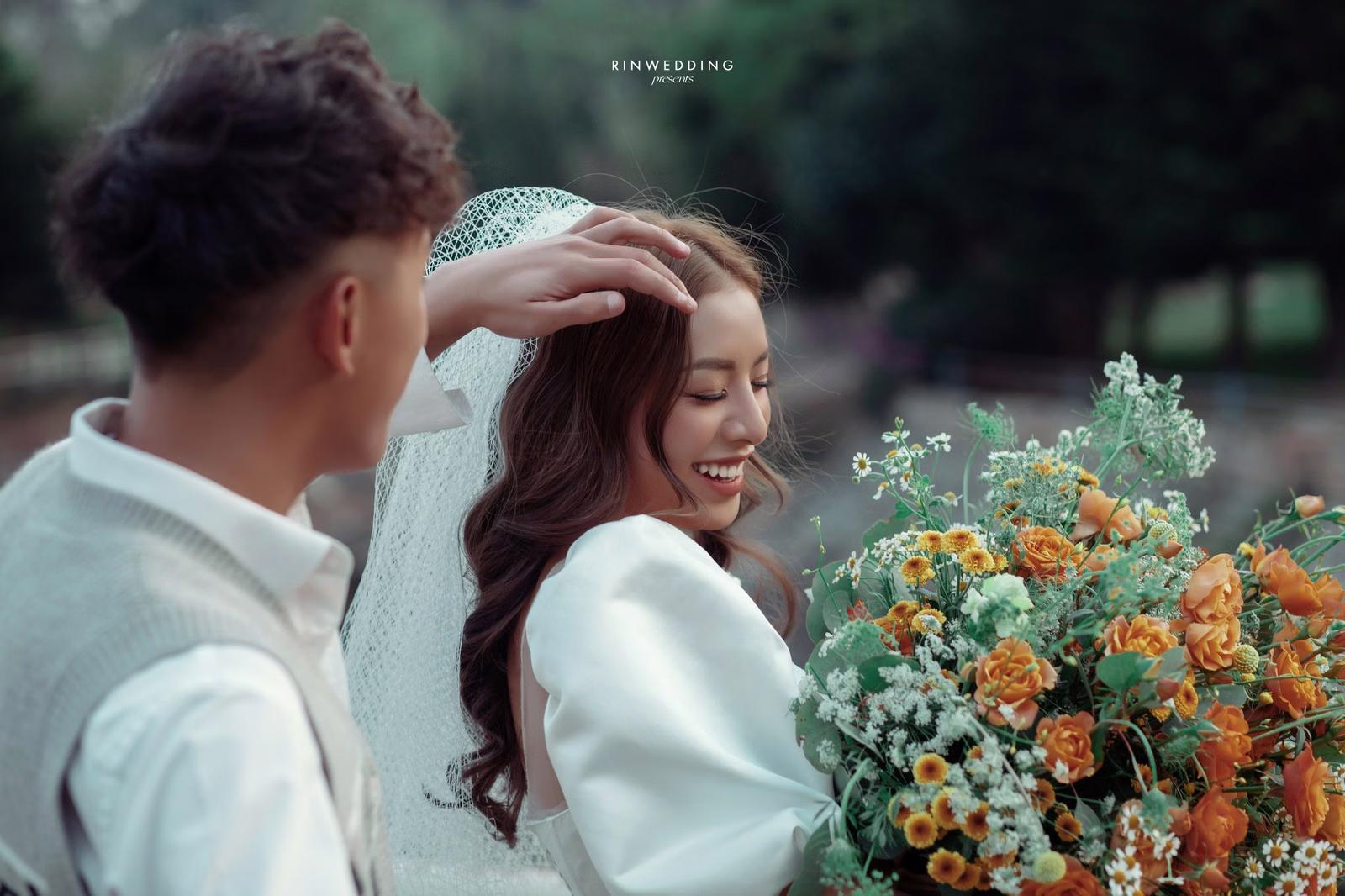 The groom adjusting the bride's veil beside an orange bouquet.