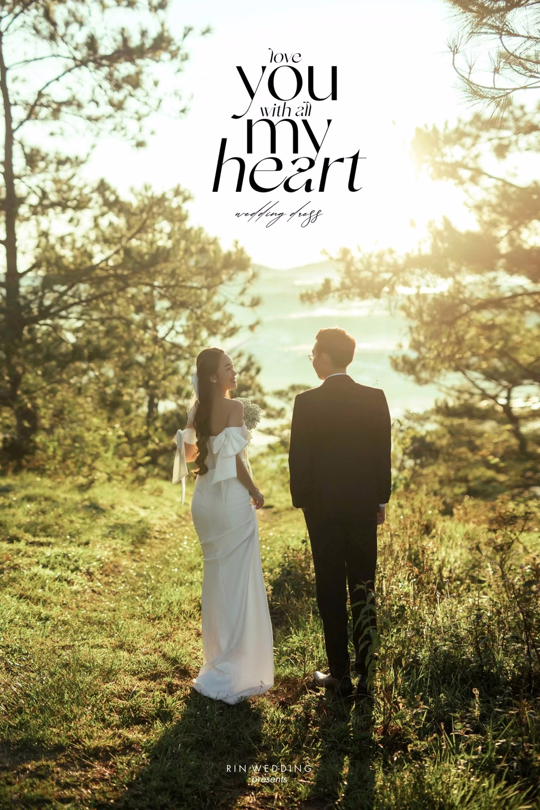 The couple stands with their backs to the camera in a sunlit pine forest at Đồi Thông Đà Lạt