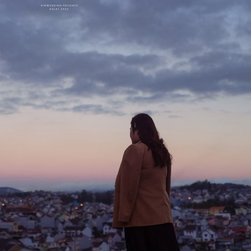 The couple looks at each other from a high viewpoint overlooking the city at dusk.