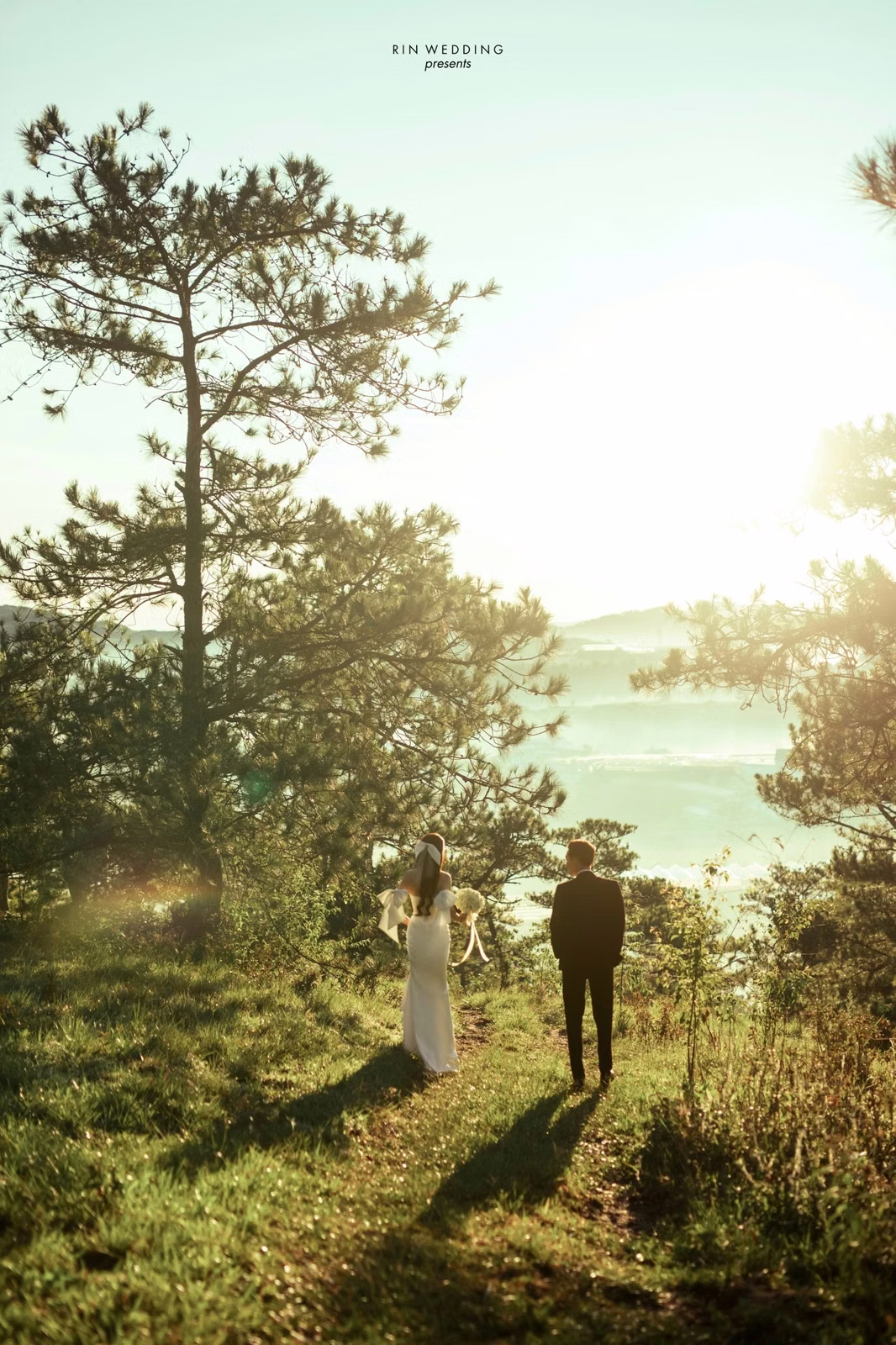 The backlit couple stands with long shadows on the grass at Đồi Thông Đà Lạt