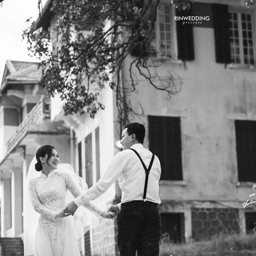 Black-and-white photograph of a bride and groom holding hands before a mansion.