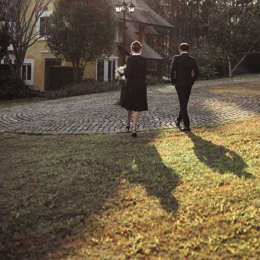 The bride and groom walking hand in hand before a sunlit villa.