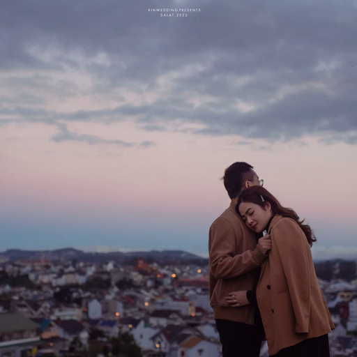 The bride rests her head on the groom's shoulder before the city at dusk.
