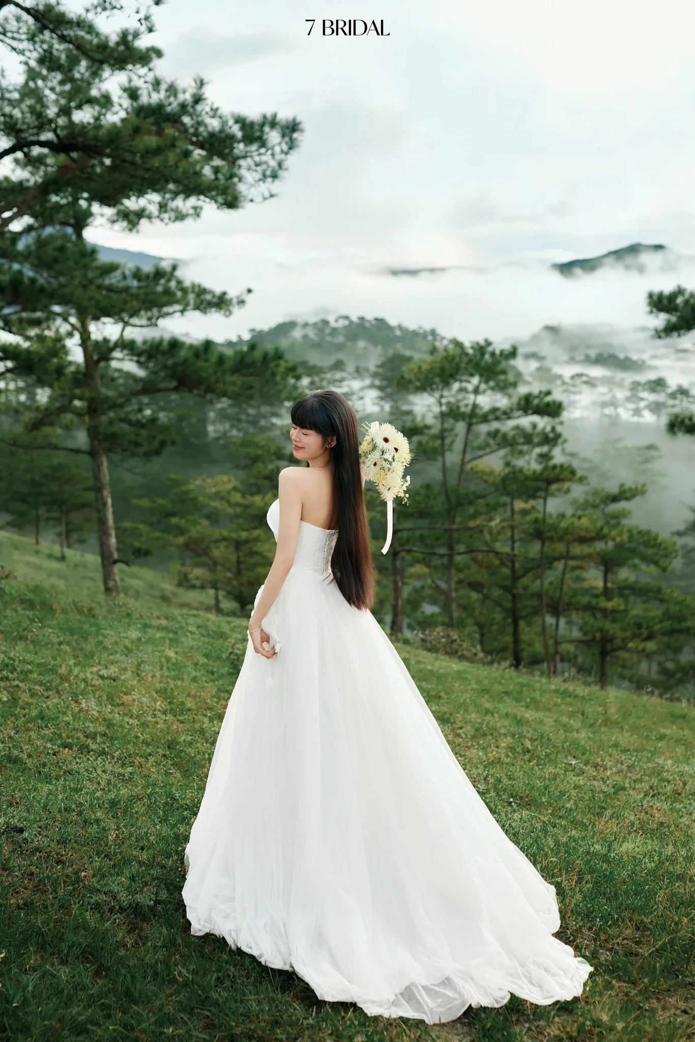 The bride looks back over her shoulder amid pine hills and clouds at Đồi Trọc Đà Lạt